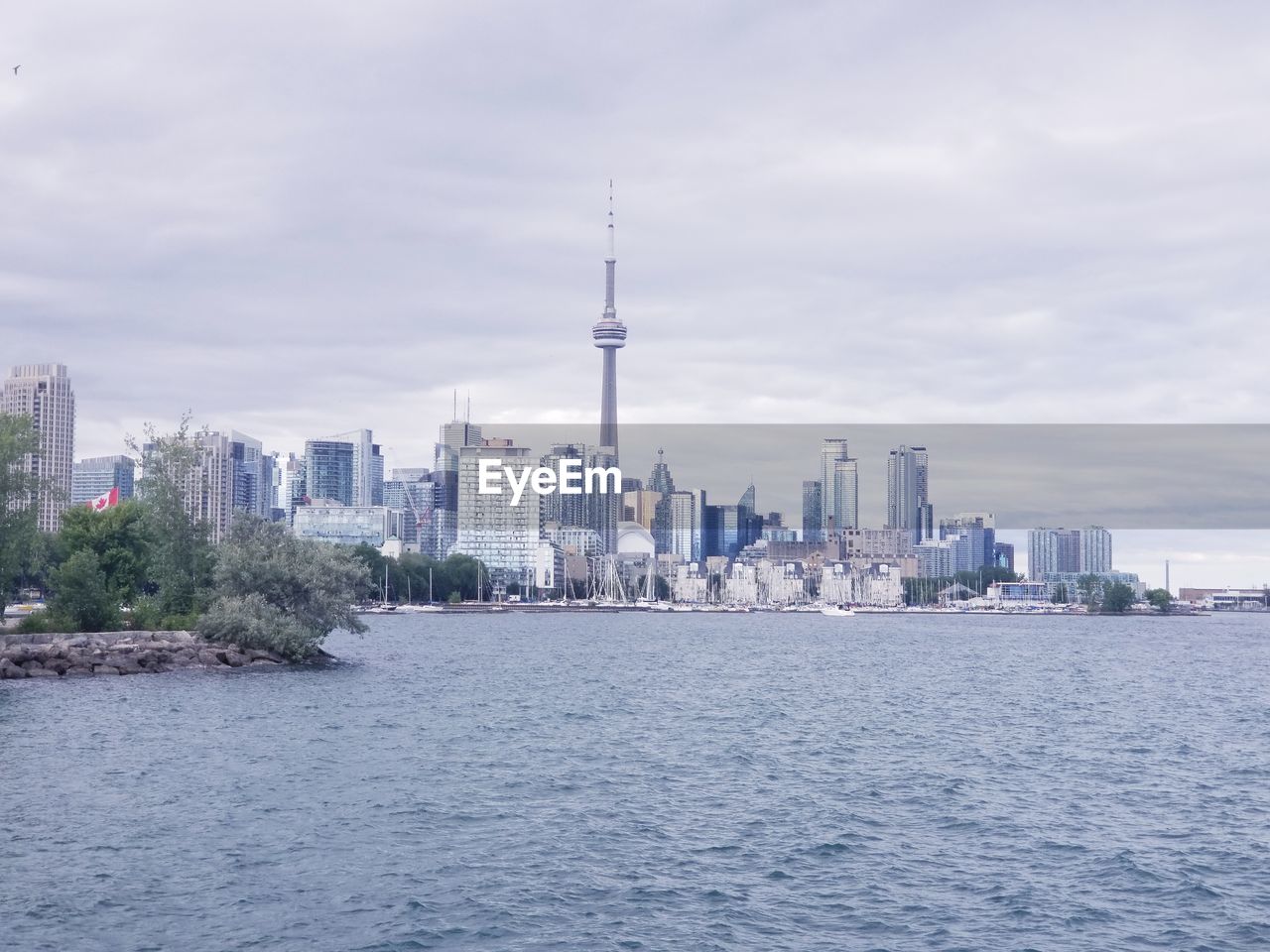 Buildings in city at waterfront against cloudy sky