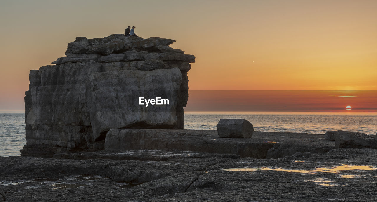 ROCK FORMATION ON SHORE AGAINST SKY AT SUNSET