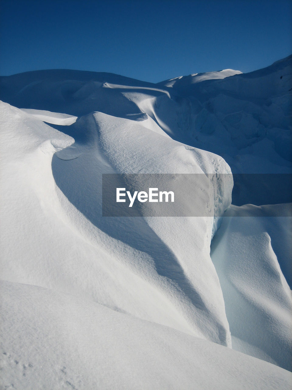 Windblown snow covering glacier ice with strong shadows, blue sky and no people on matanuska glacier