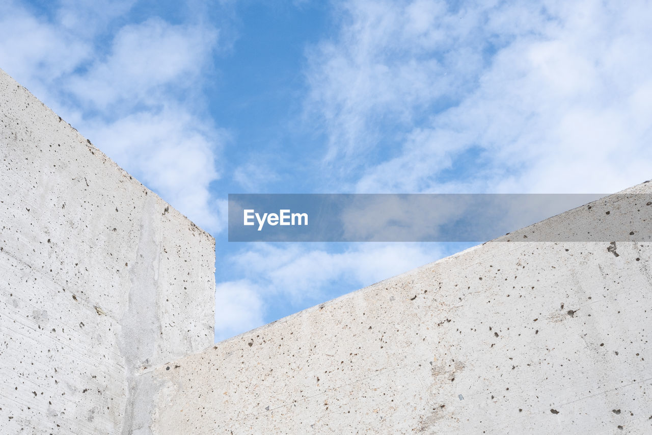 Low angle view of concrete wall against cloudy sky