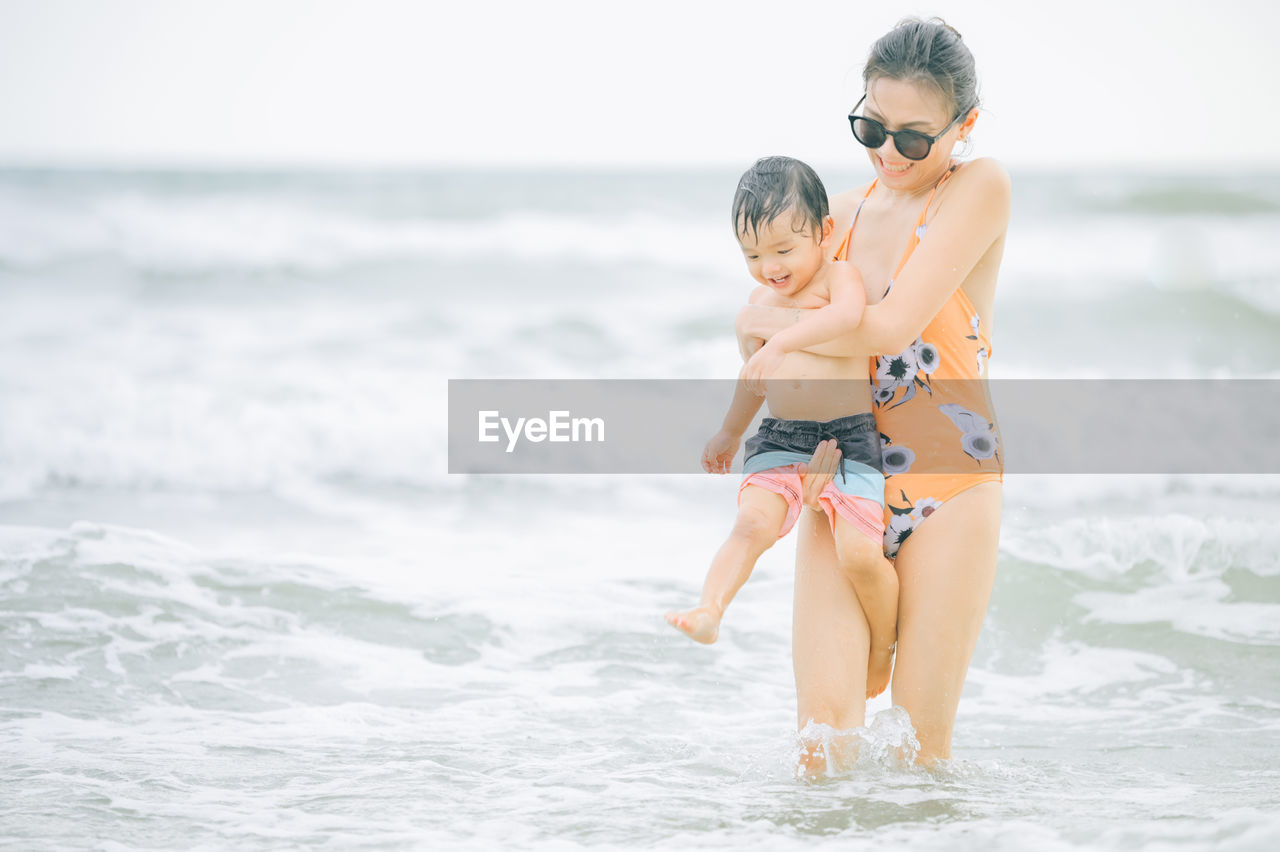 Smiling mother with son enjoying on sea water