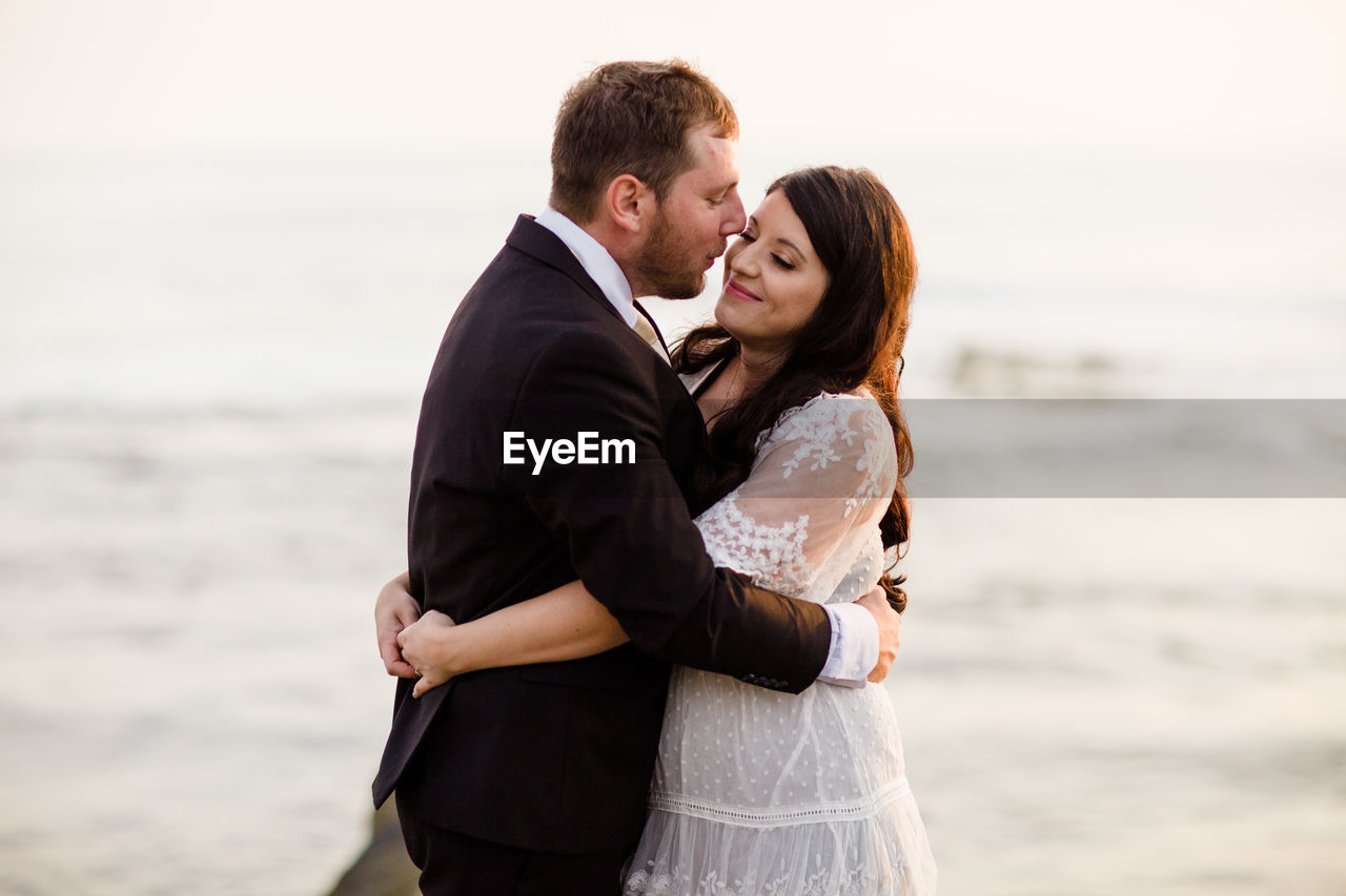 Newlyweds standing on rock at beach in san diego during sunset