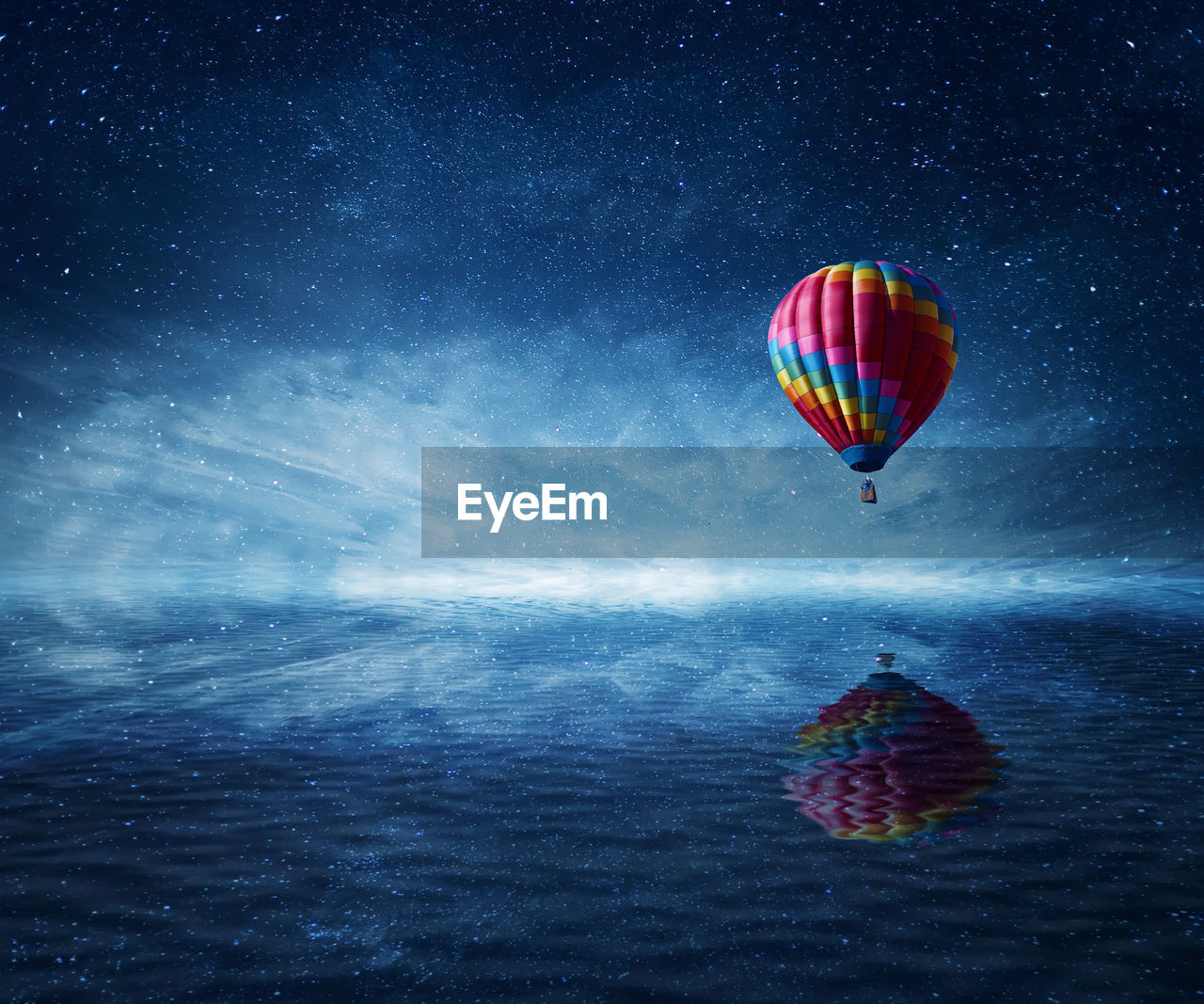 Hot air balloon flying over sea against blue startul night sky