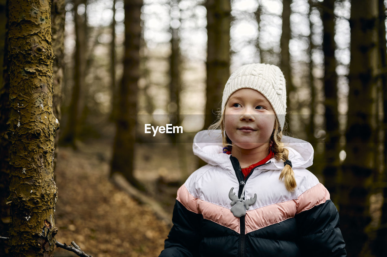 Positive child in warm clothes relaxing in autumn forest