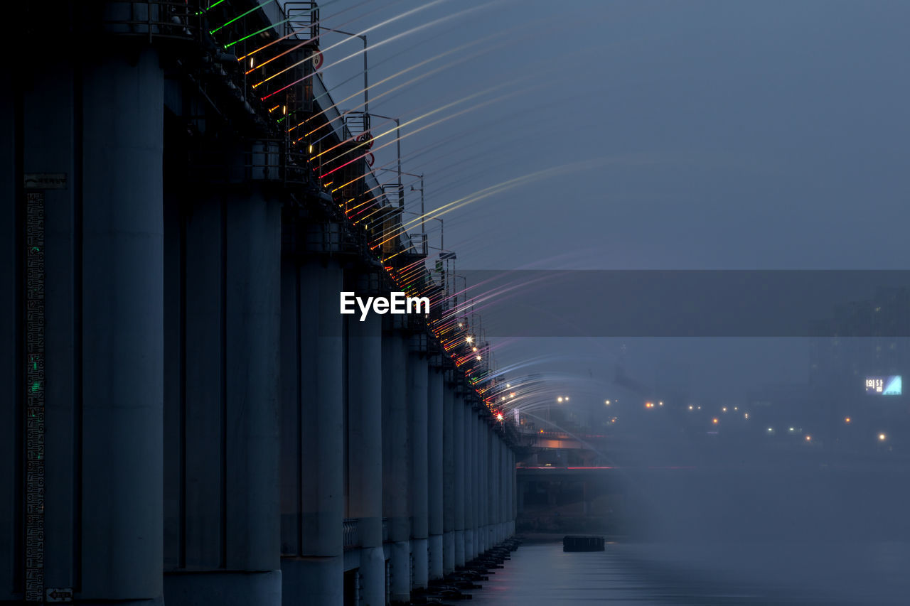 Low angle view of water flowing from bridge in river against sky at dusk