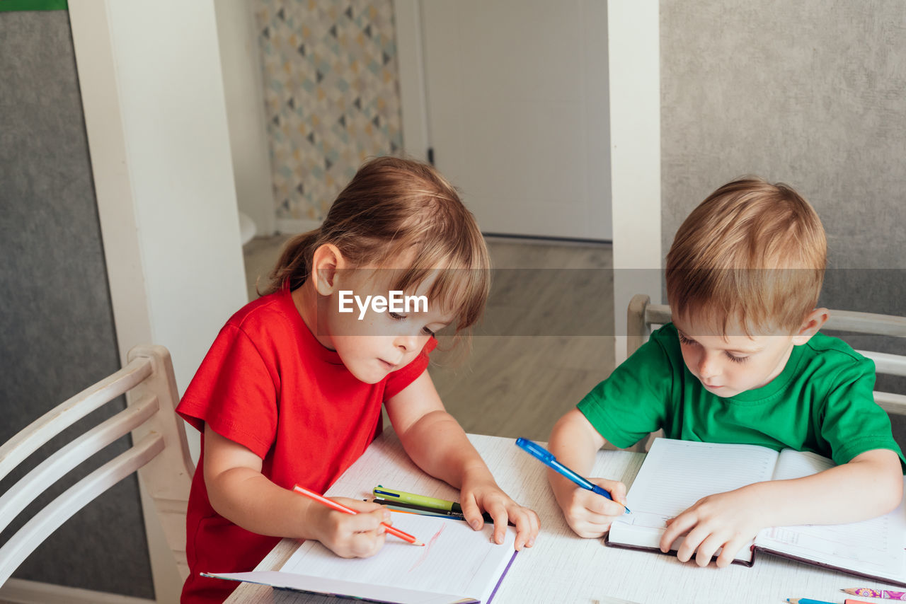 Children sit at the table and write in notebooks. homeschooling concept, learning online