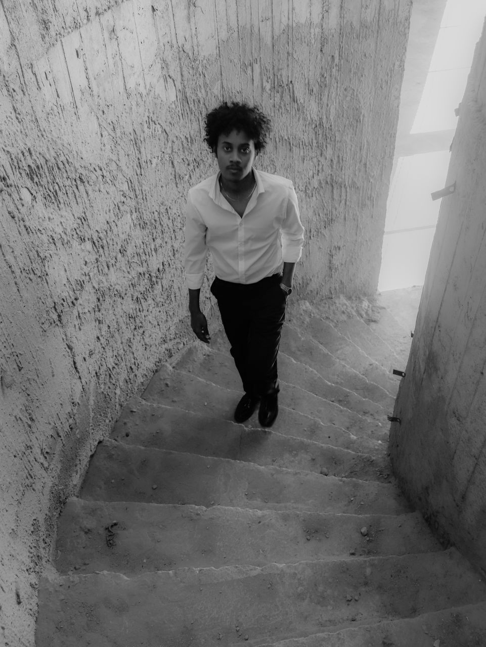 white, black, one person, full length, black and white, architecture, front view, staircase, monochrome, young adult, monochrome photography, casual clothing, wall - building feature, lifestyles, leisure activity, steps and staircases, portrait, adult, looking at camera, built structure, snapshot, standing, day, men, fashion, sitting, footwear, outdoors