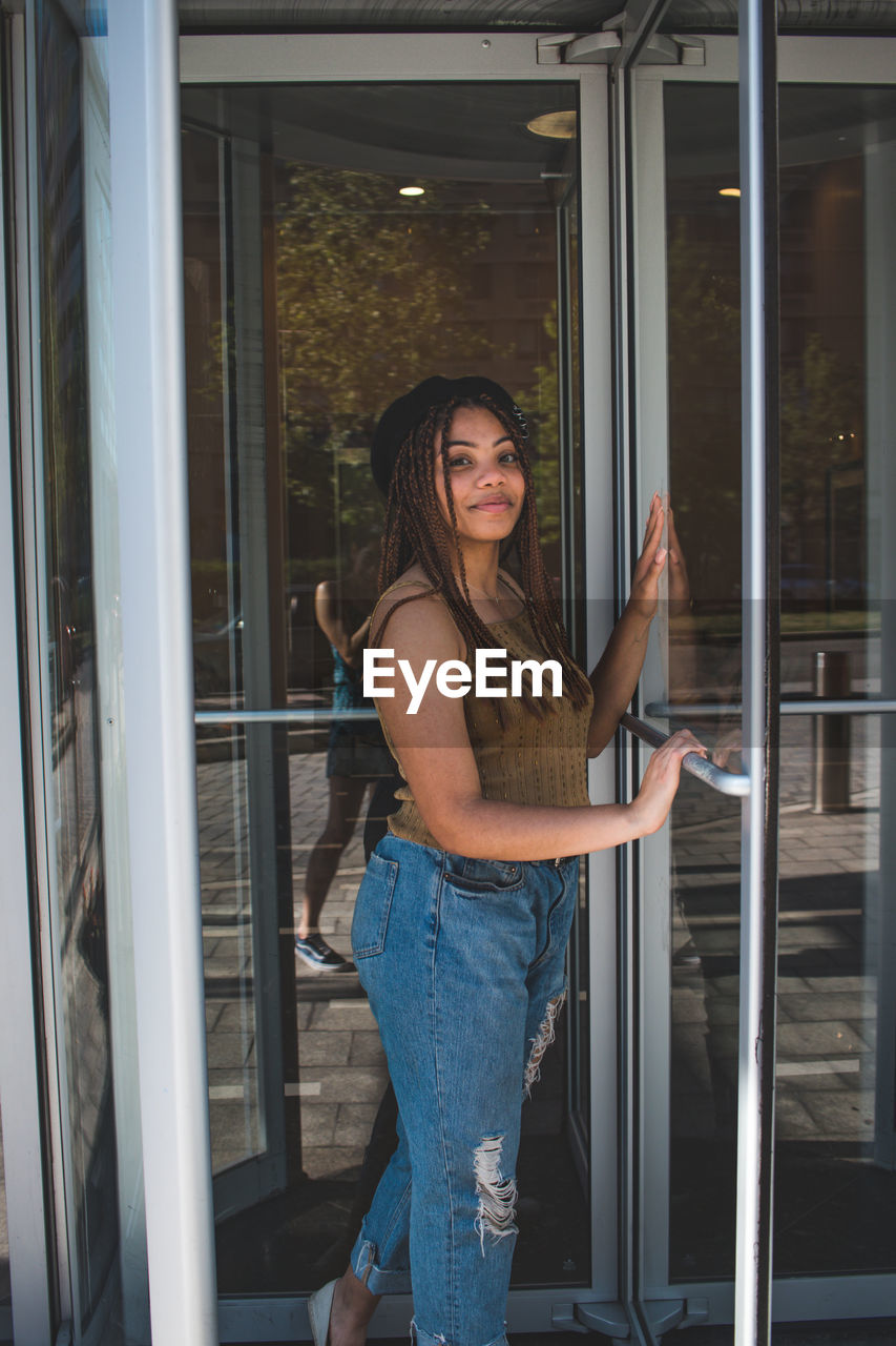 PORTRAIT OF BEAUTIFUL WOMAN STANDING BY WINDOW