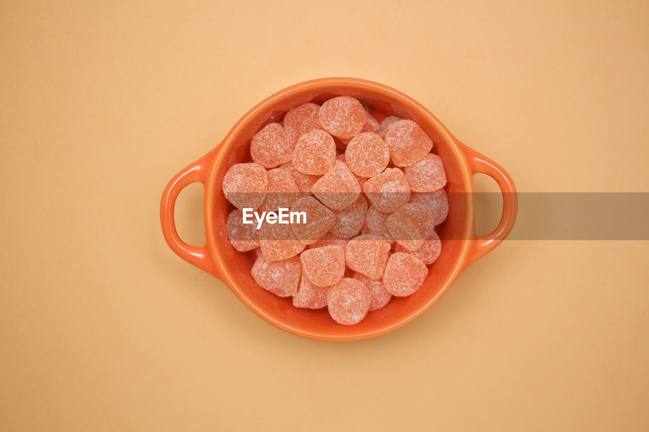 Directly above view of candies in bowl on beige background
