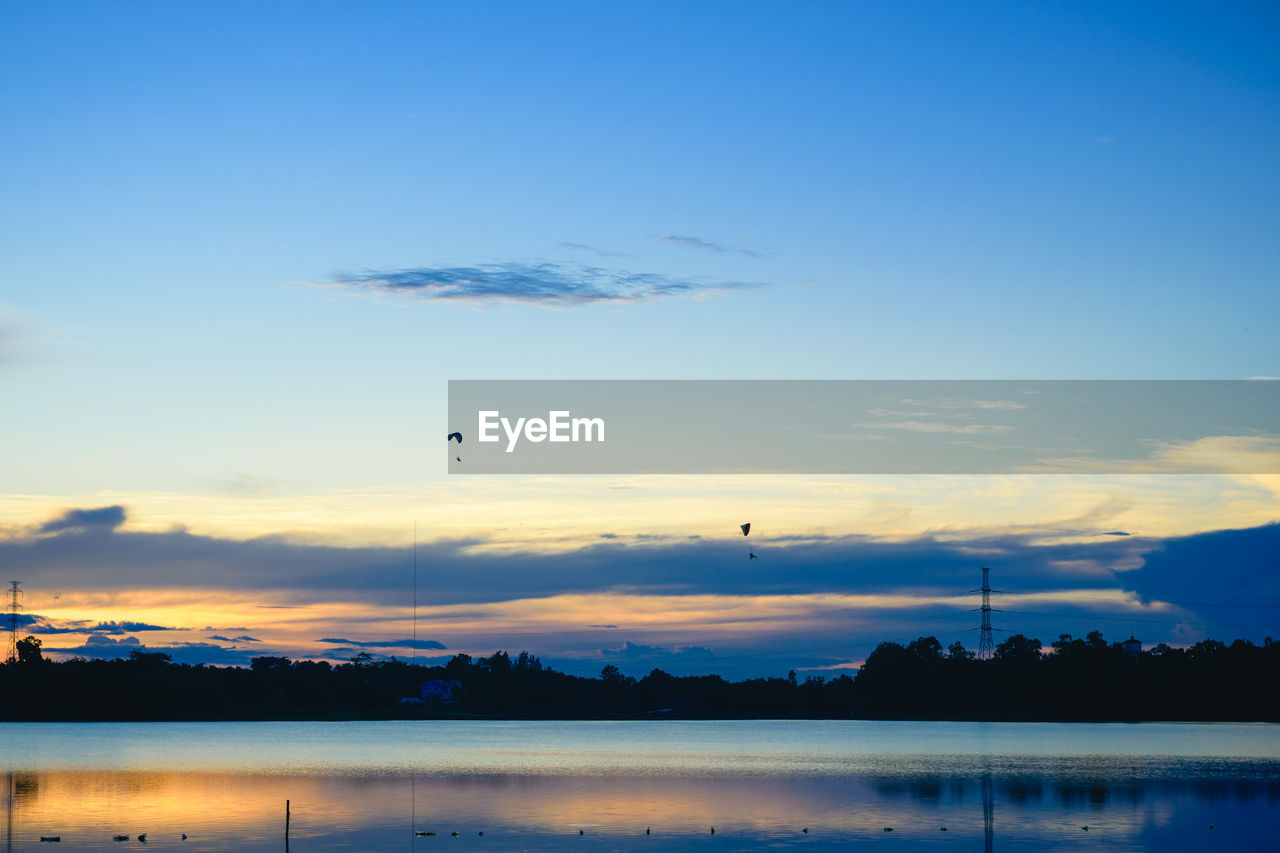 Silhouette paramotor pilots flying over a lake with the sunset sky background