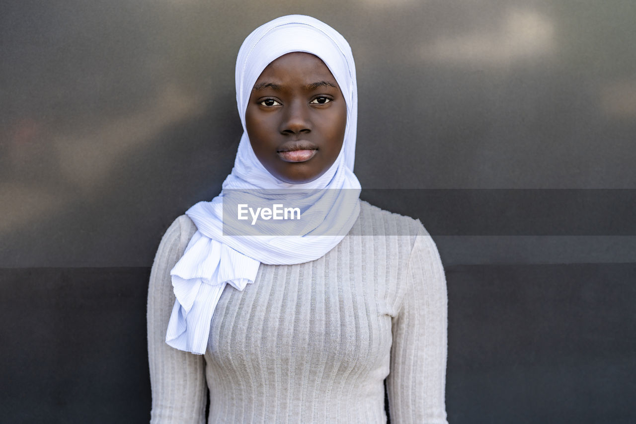 Young woman with hijab standing in front of gray and black wall