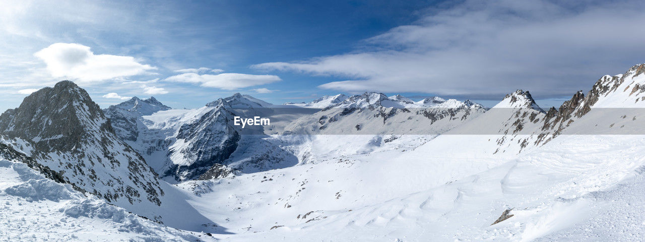 snow, cold temperature, winter, mountain, scenics - nature, environment, sky, landscape, beauty in nature, cloud, mountain range, nature, snowcapped mountain, travel destinations, ski touring, panoramic, piste, tranquil scene, ski mountaineering, travel, white, tranquility, no people, mountain peak, blue, land, outdoors, ridge, day, non-urban scene, frozen, ice, extreme terrain, forest, sports, winter sports, massif, holiday, tourism, coniferous tree, sunlight, idyllic