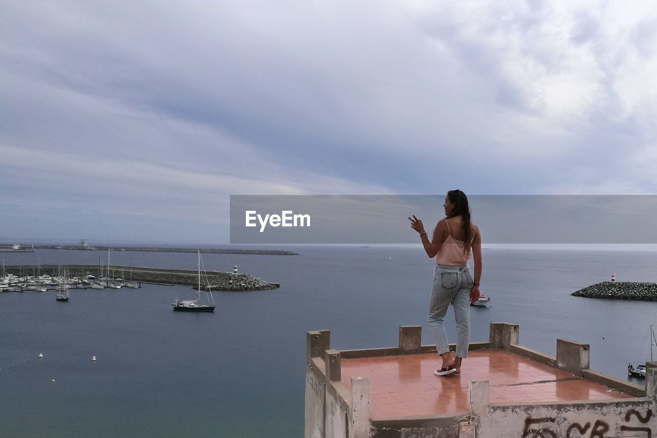 Woman standing on building terrace against sea against sky