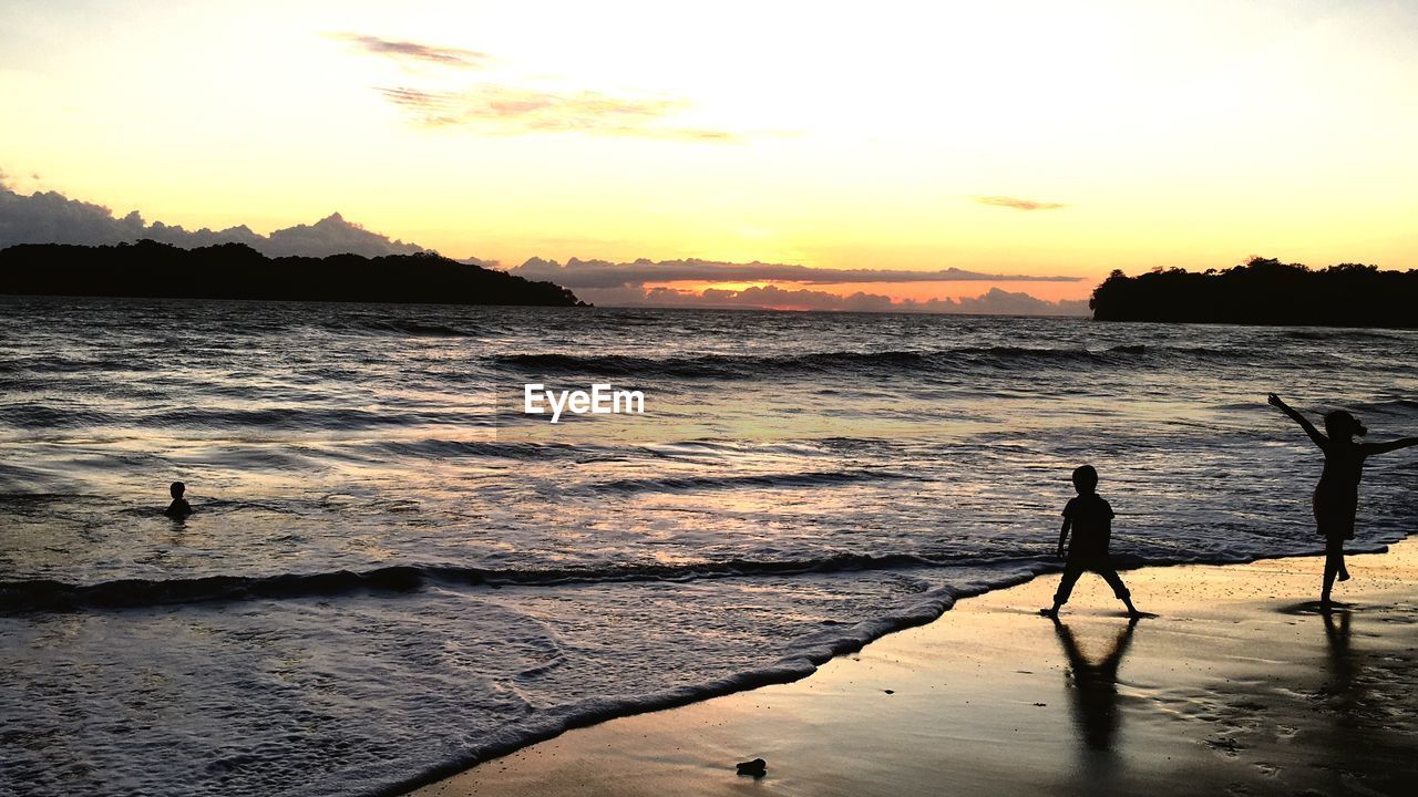 SILHOUETTE PEOPLE STANDING ON BEACH DURING SUNSET