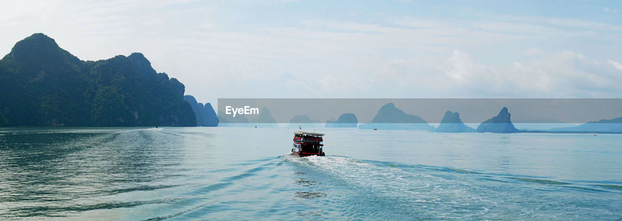 water, nature, transportation, sky, sea, nautical vessel, scenics - nature, beauty in nature, travel, mountain, vehicle, travel destinations, landscape, panoramic, land, bay, cloud, environment, boat, outdoors, boating, day, mode of transportation, ocean, holiday, tranquility, vacation, trip, coast, tourism, tranquil scene, adventure, beach, blue, mountain range, one person, bay of water, ship