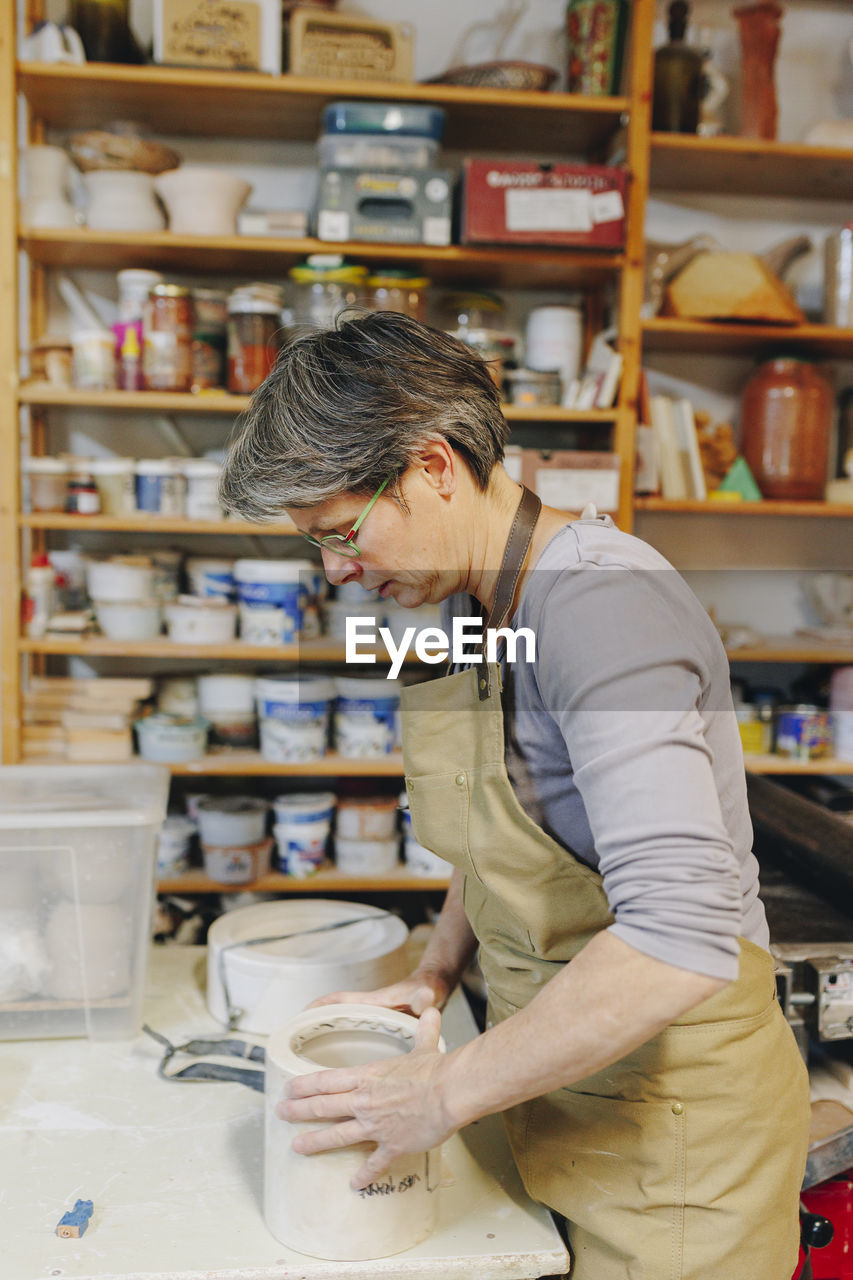 Mature potter with ceramics working at workshop