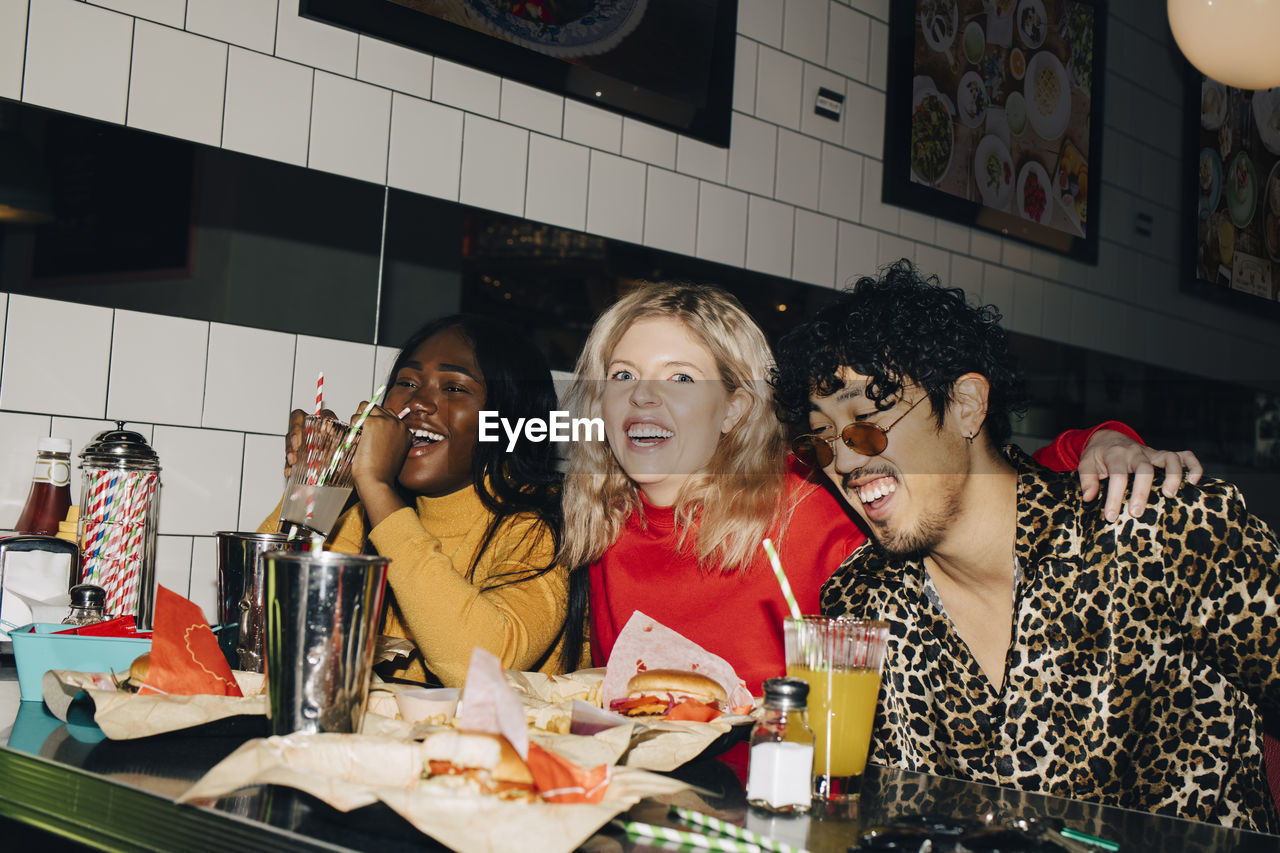 Portrait of happy woman with friends eating burger during social gathering at cafe