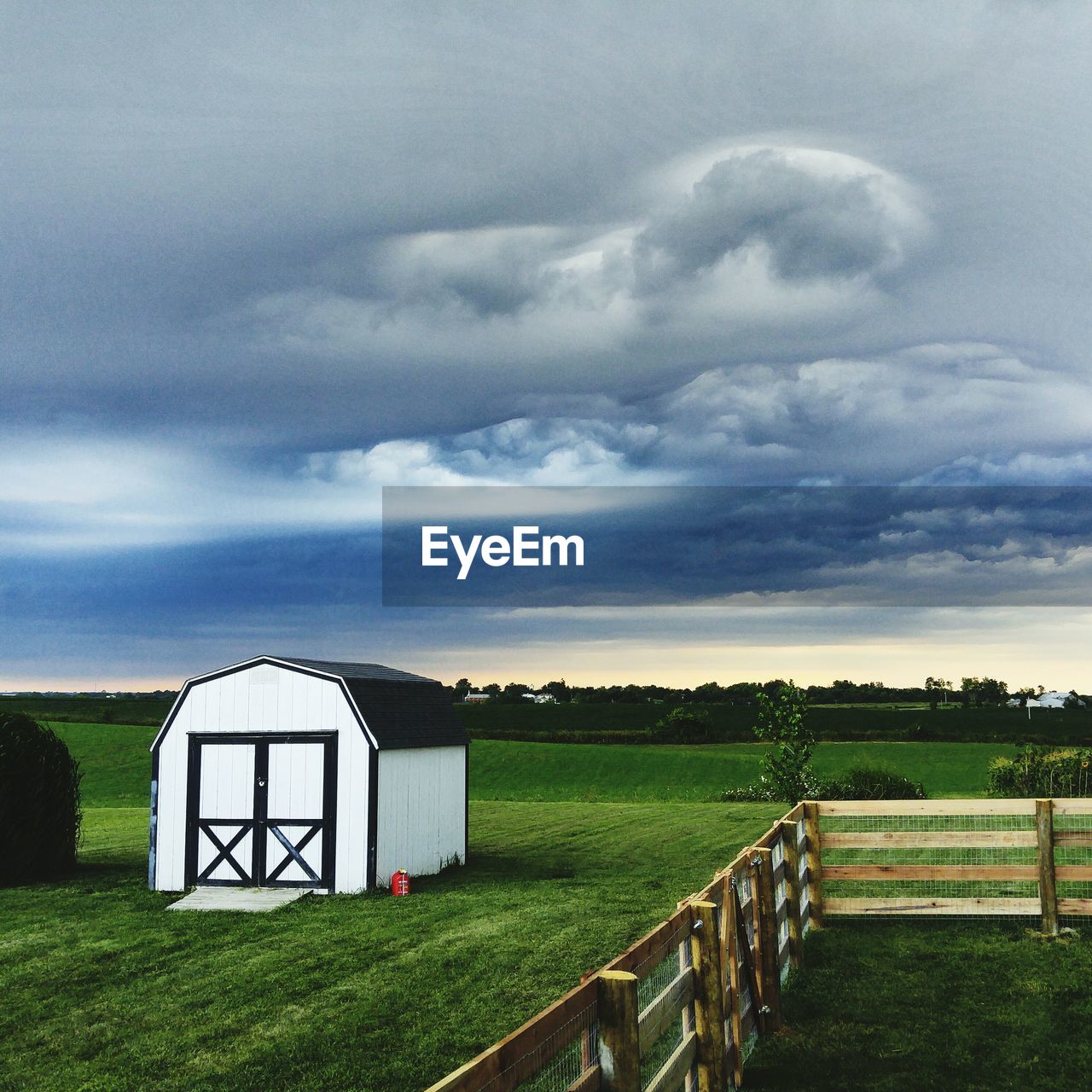 Barn on grassy field against cloudy sky