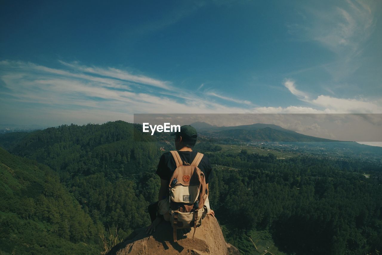 Rear view of man sitting against mountains on rock