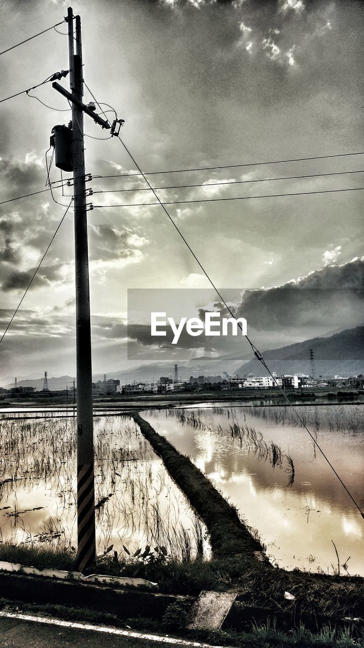 ELECTRICITY PYLON ON RIVERBANK AGAINST SKY