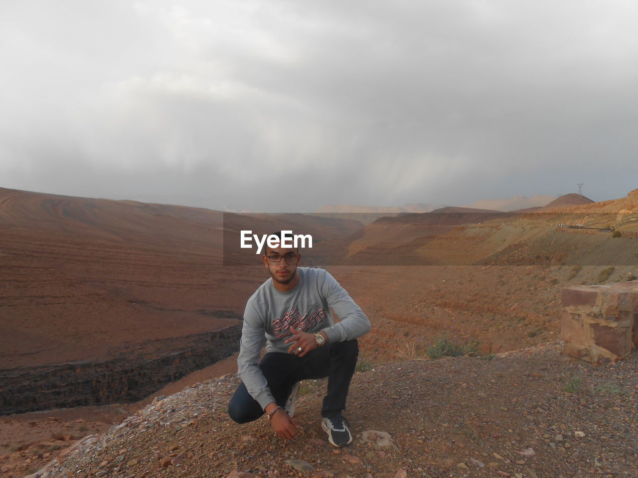 MAN SITTING ON MOUNTAIN AGAINST SKY