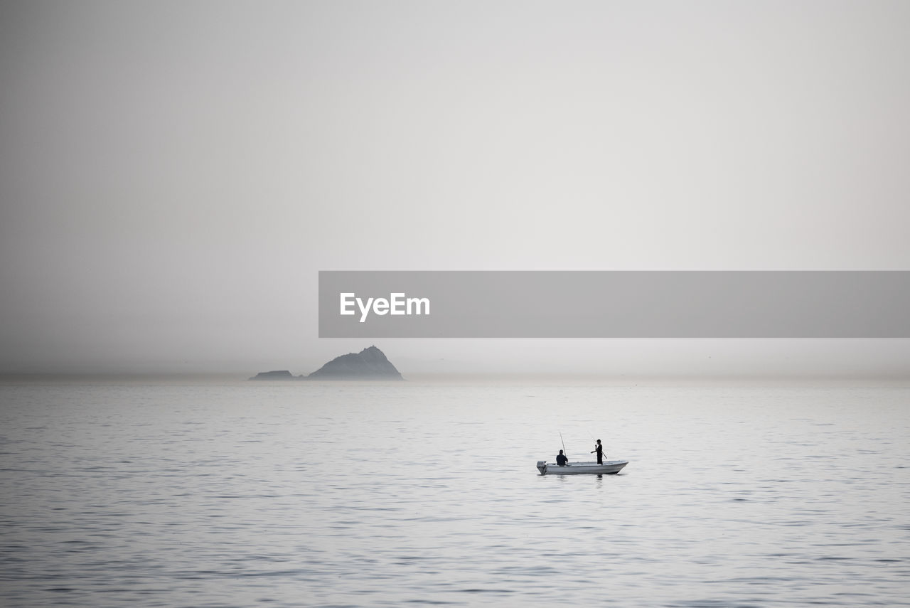 Silhouette men on boat over sea during foggy weather