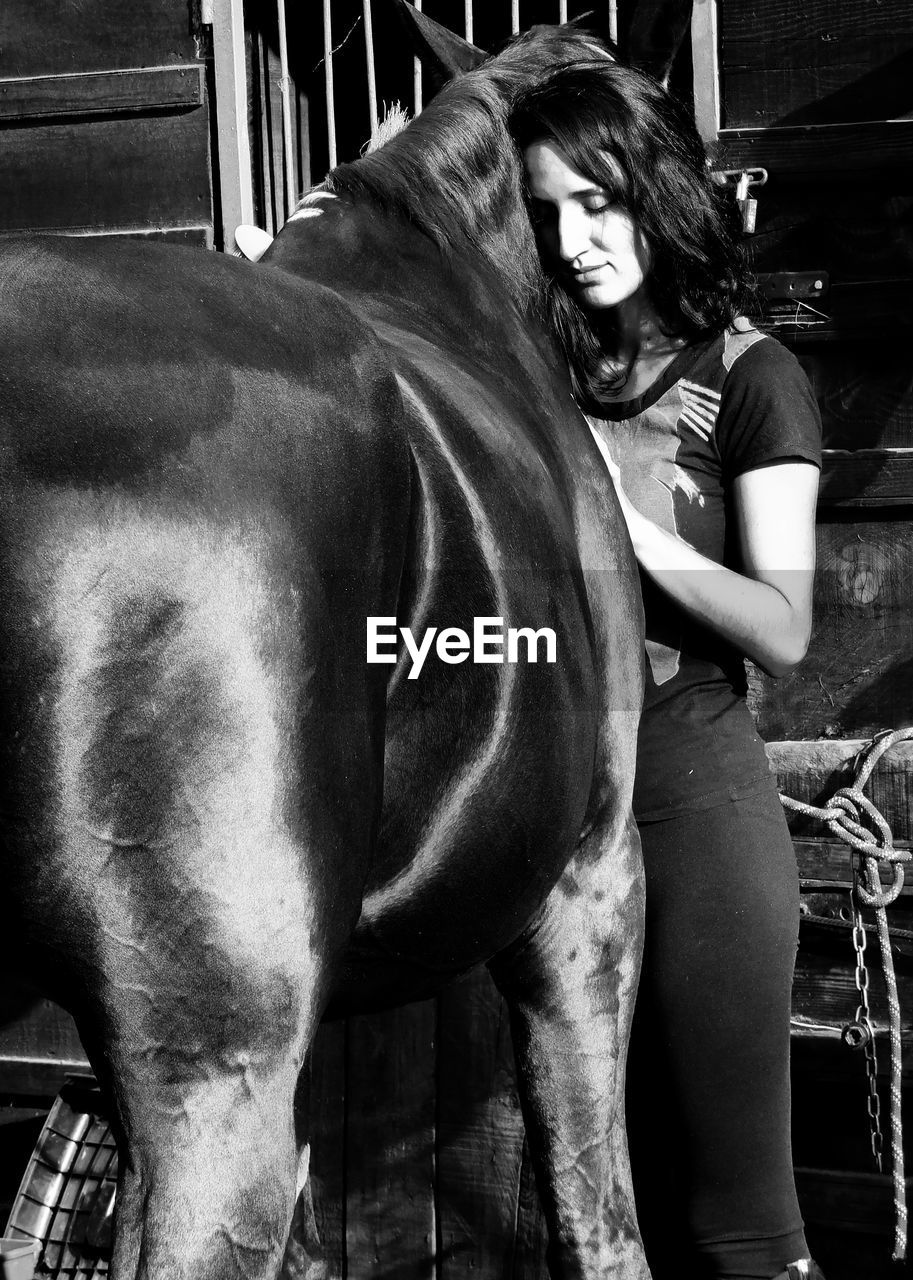 Young woman embracing horse while standing at stable