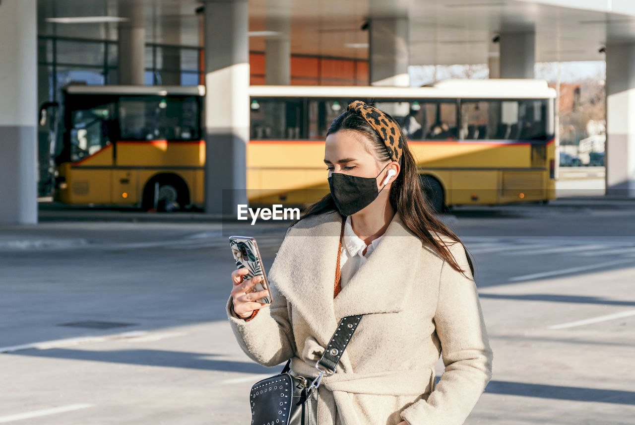 Young woman wearing black face mask in city. using mobile phone, covid, corona.
