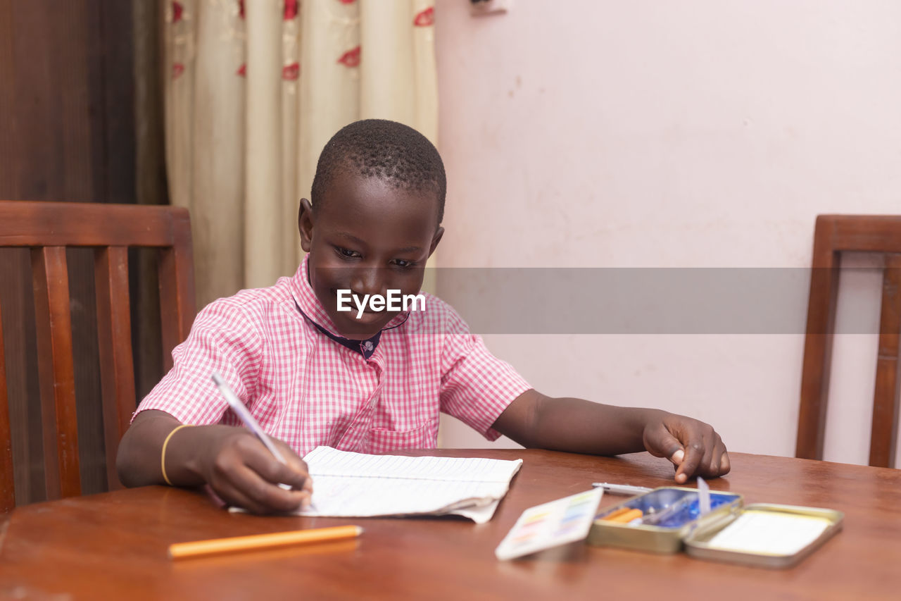 Portrait of young african schoolboy focused smiling writing on paper