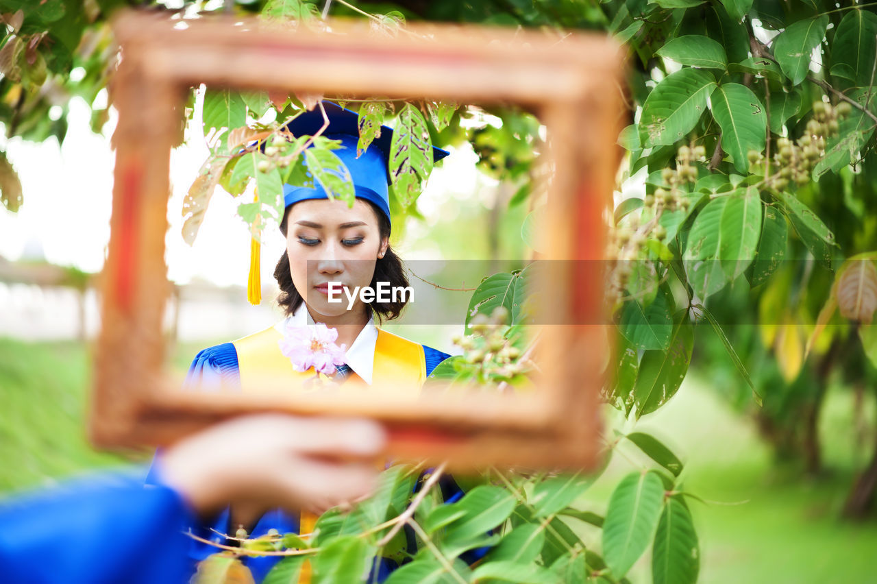 Cropped hand of woman holding mirror with her reflection against tree