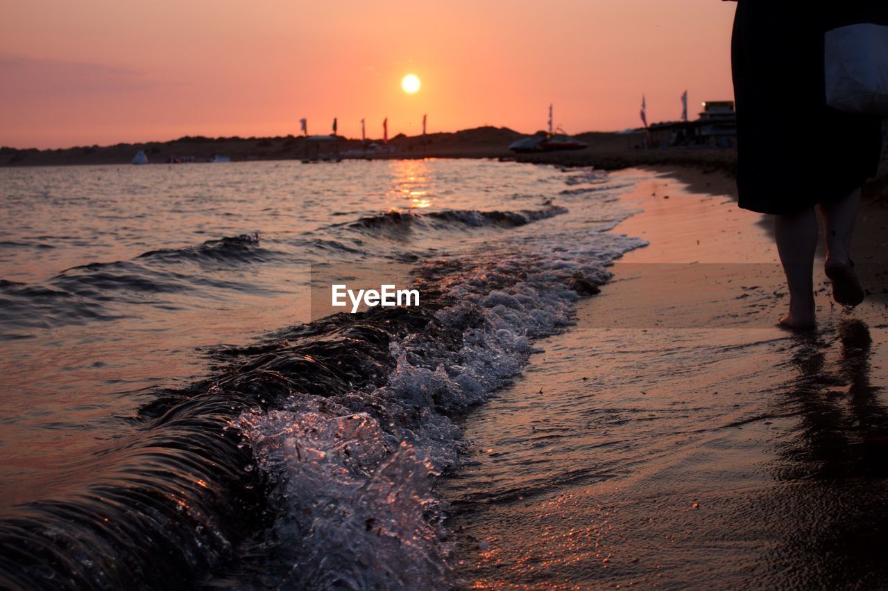 Rear view of woman walking at beach during sunset