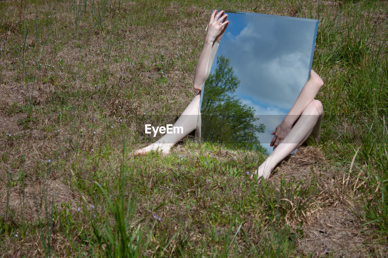 Woman holding mirror with reflection while sitting on grass