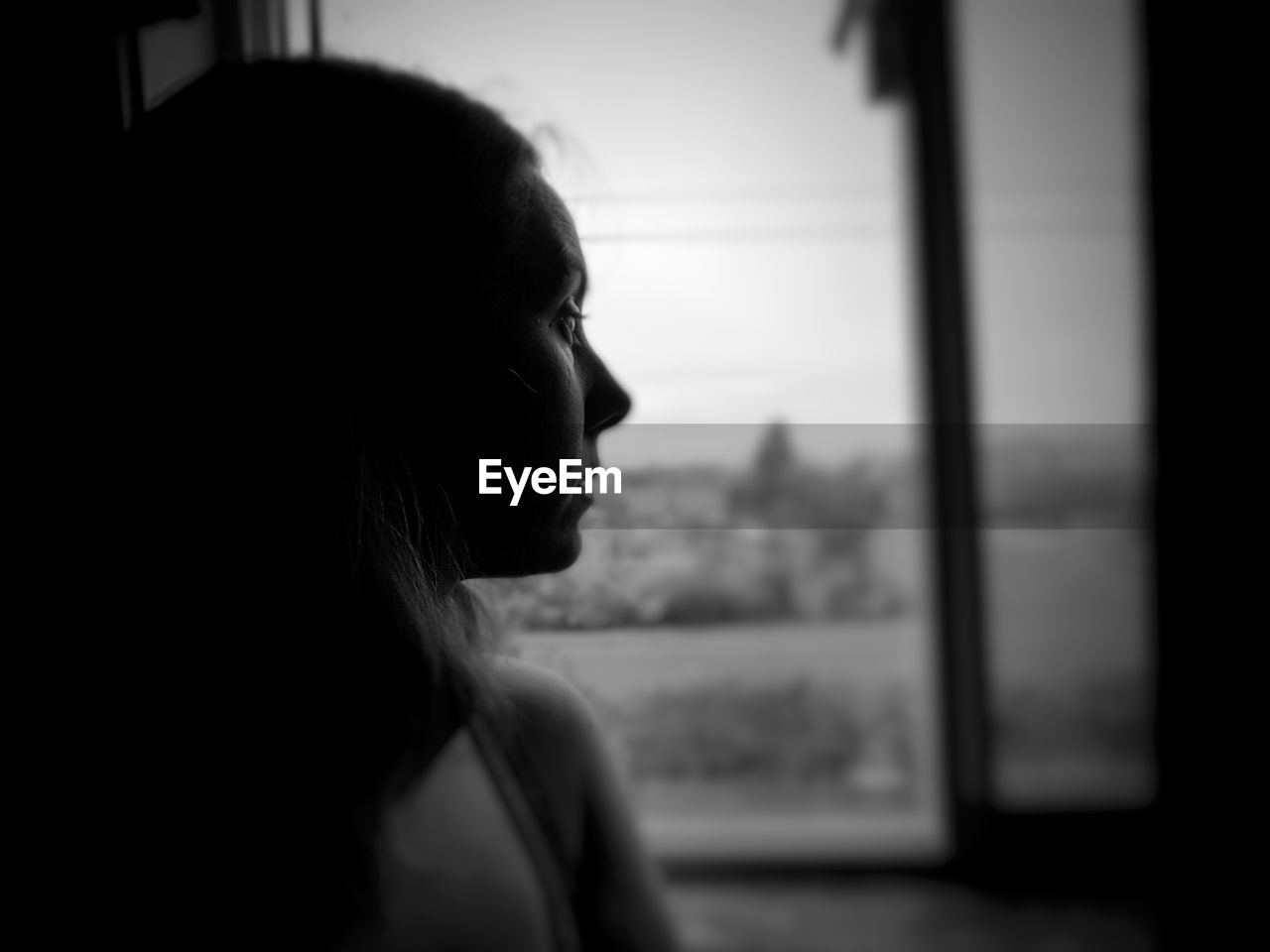 CLOSE-UP PORTRAIT OF WOMAN LOOKING THROUGH WINDOW AT HOME