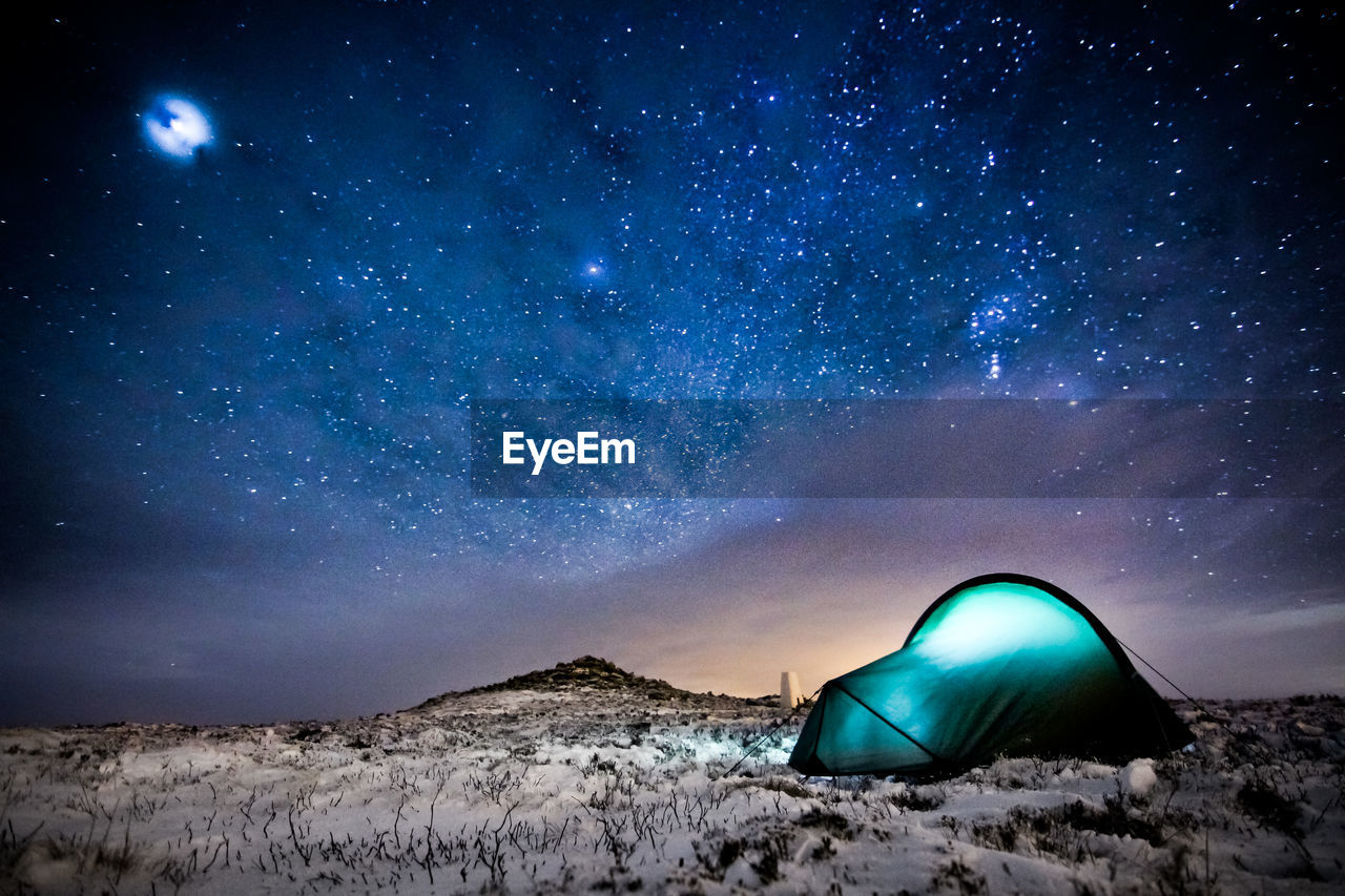 Illuminated tent on snow covered field at night