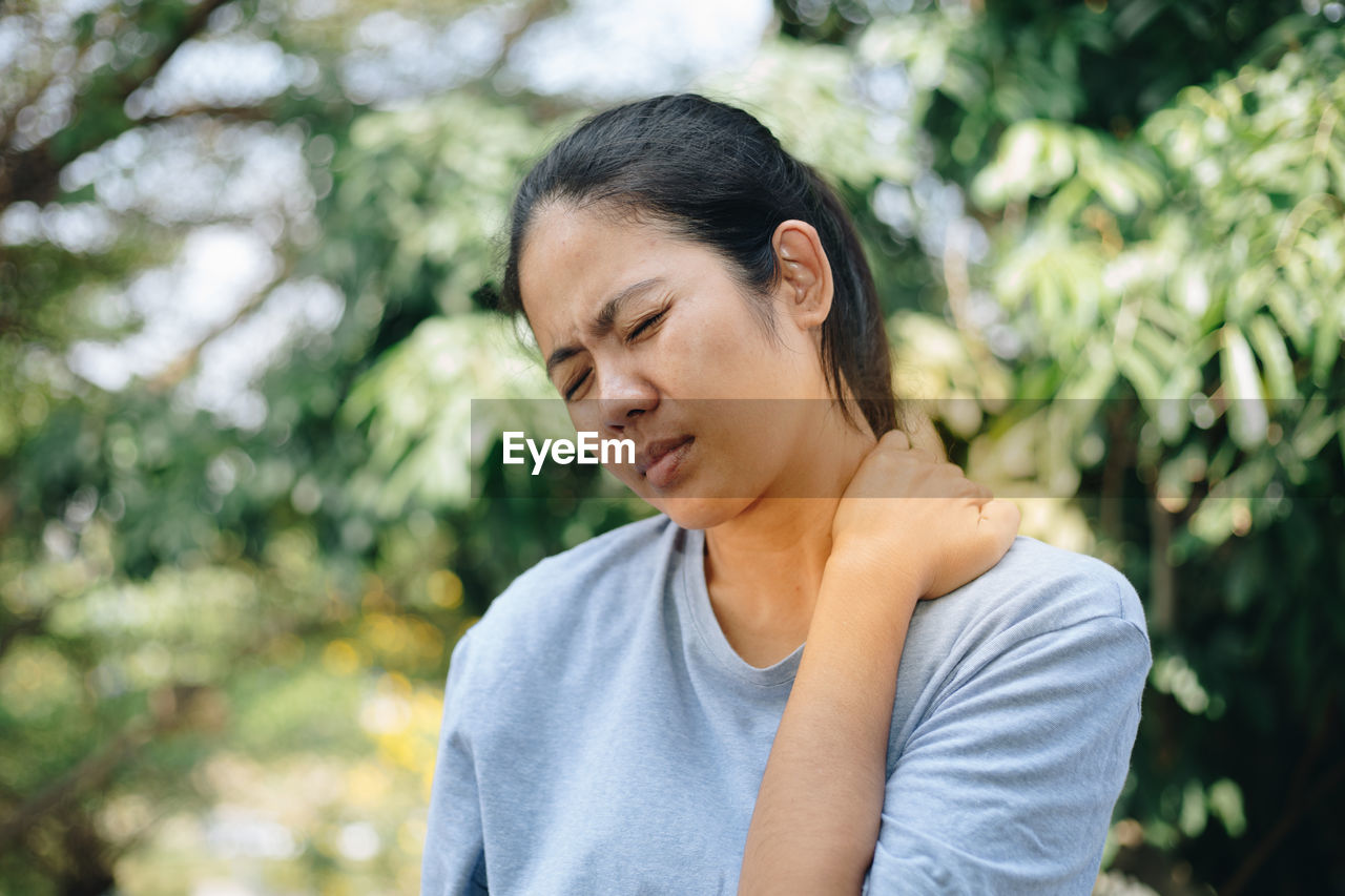 Woman touching neck in pain against trees