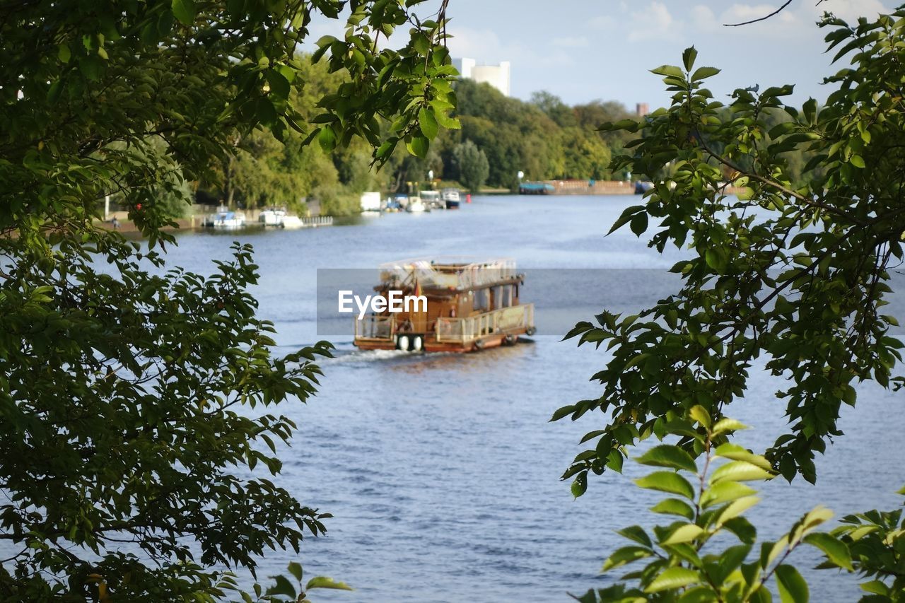 Boat moving on river with trees in foreground