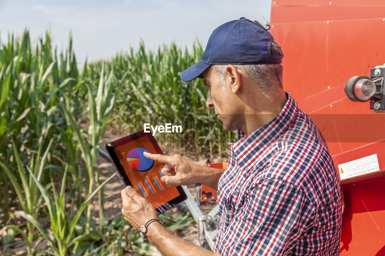 Side view of man pointing at chart in digital tablet while standing at farm