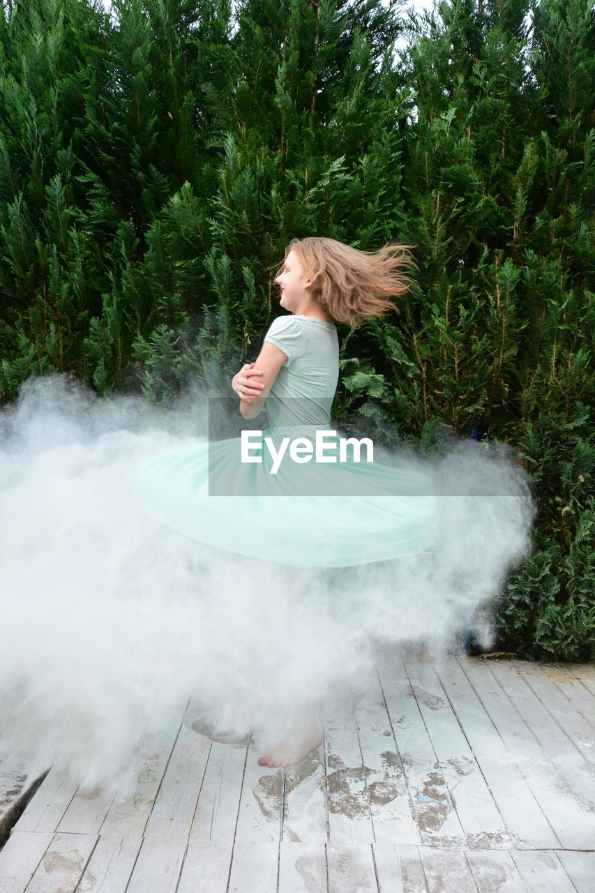 Side view of happy girl spinning with smoke against plants at park