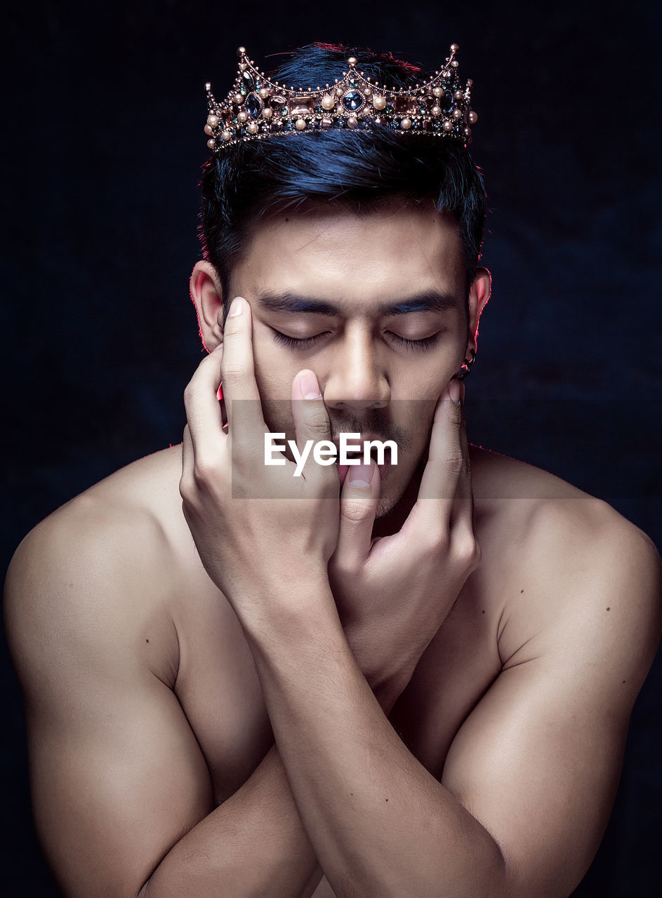 Close-up of young man wearing crown against black background