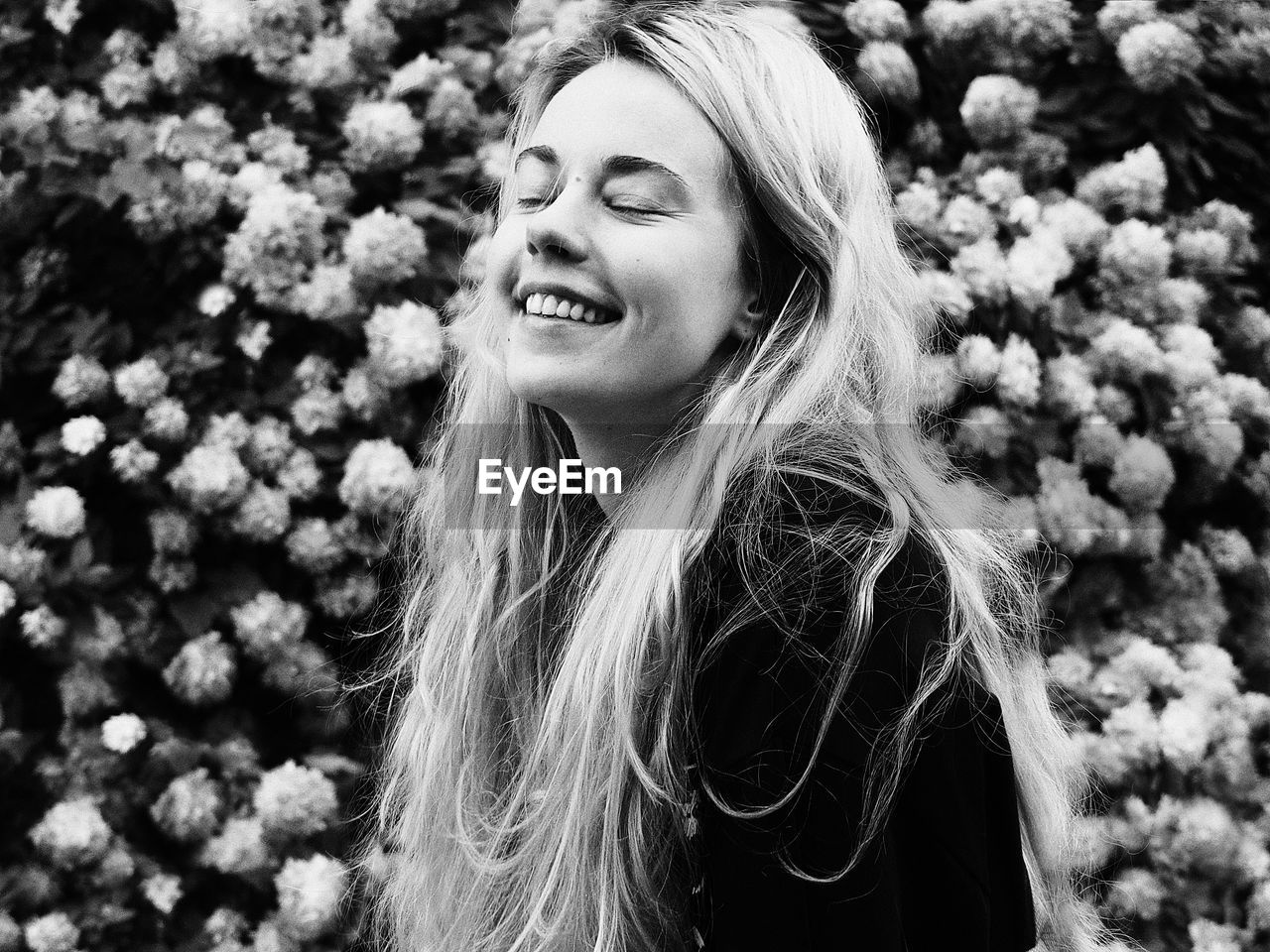 Close-up of smiling young woman against white flowering plants