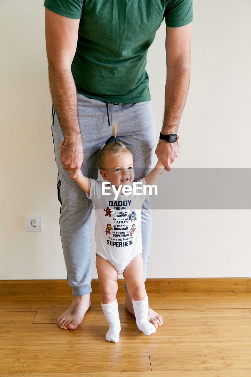 Low section of father with daughter standing by wall at home