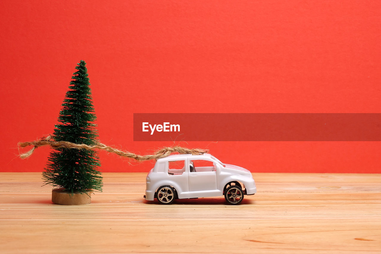 Close-up of christmas tree by toy car on table against red background