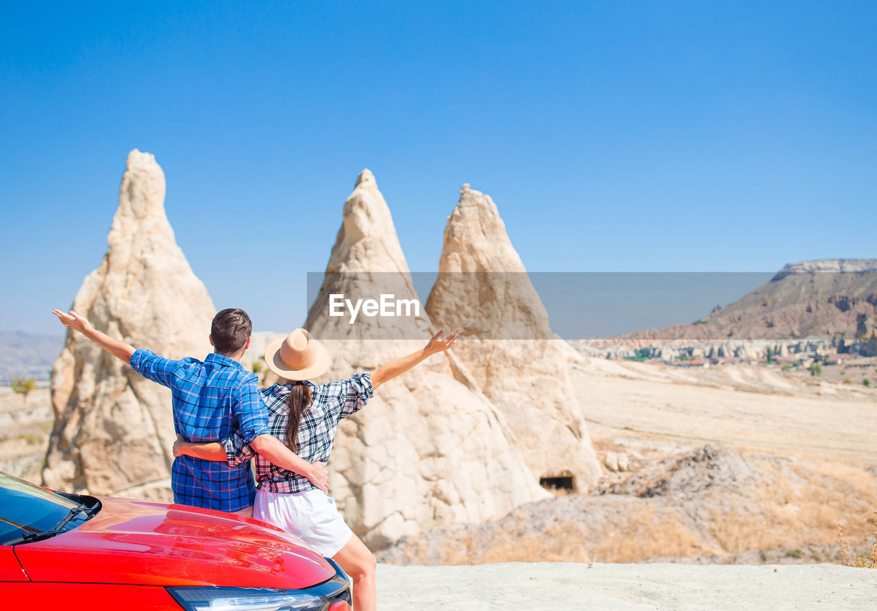 rear view of woman sitting on rock against clear blue sky