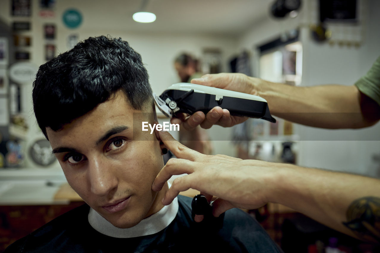 A young boy looking at the camera while having his hair cut by machine