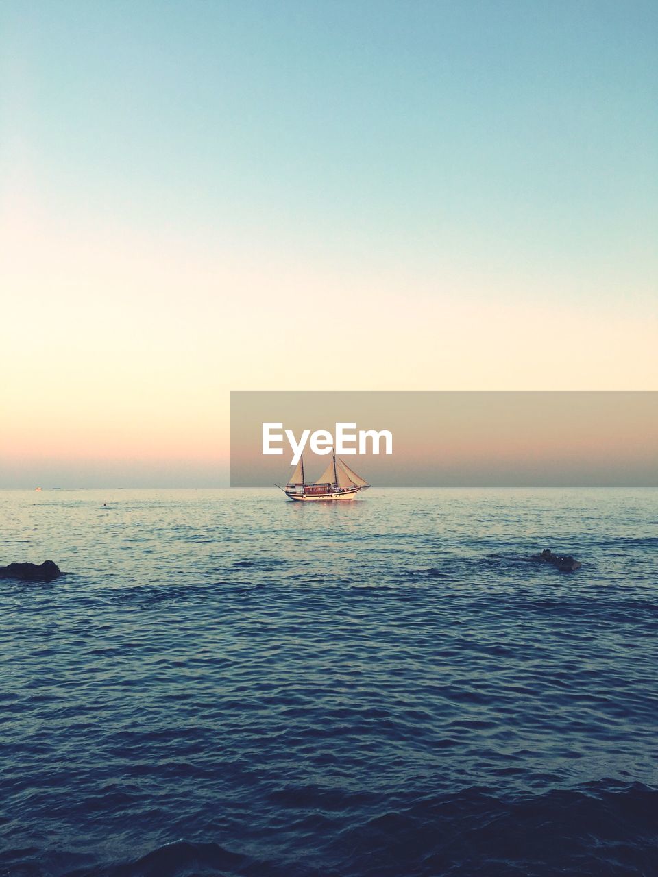 Distant image of ship sailing in sea against sky during sunset