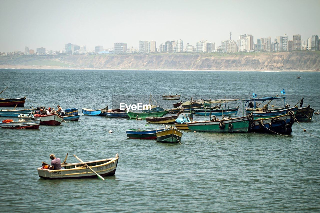 High angle view of fishing boats in water by buildings against sky