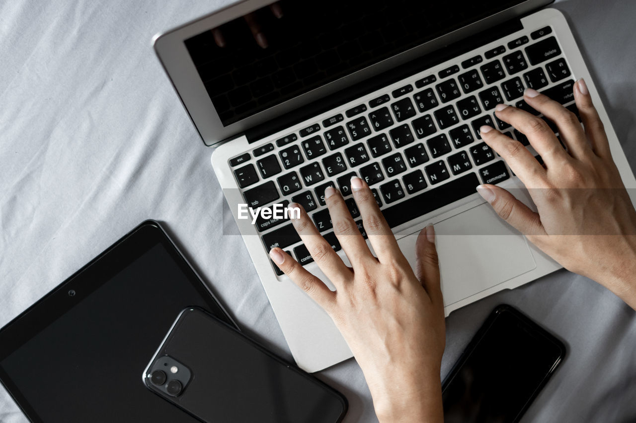 Cropped hands of woman using laptop on bed