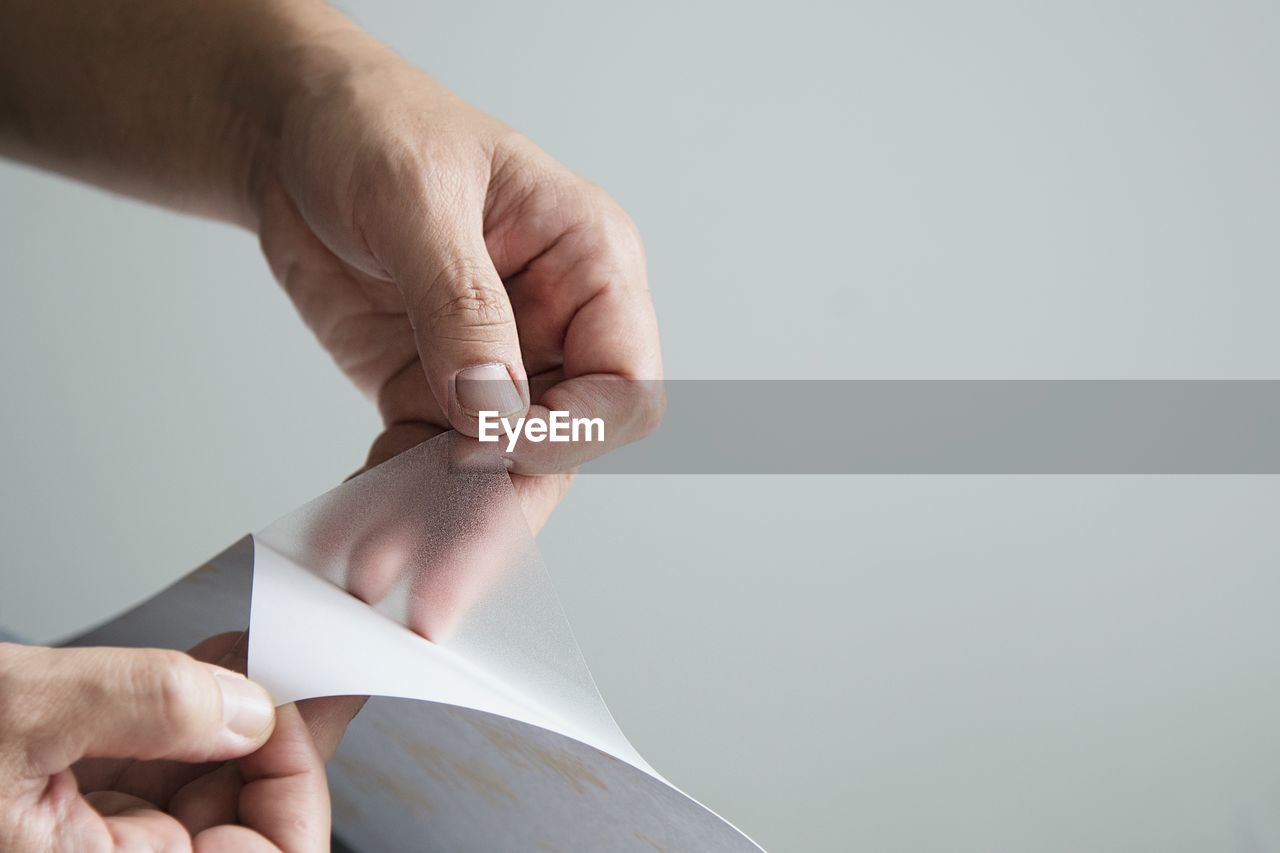 CLOSE-UP OF PERSON HOLDING PAPER AGAINST WHITE BACKGROUND