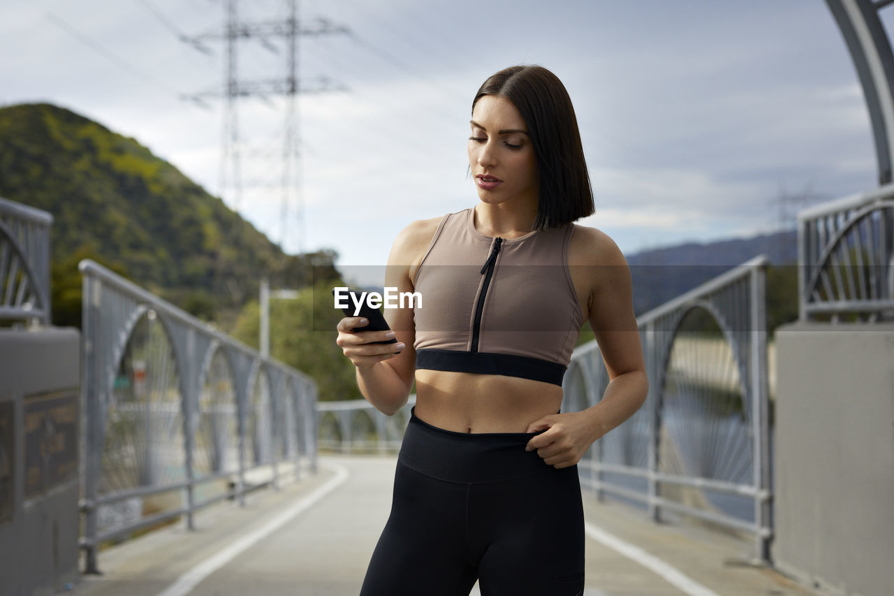 Woman in sportswear using smart phone while standing on bridge