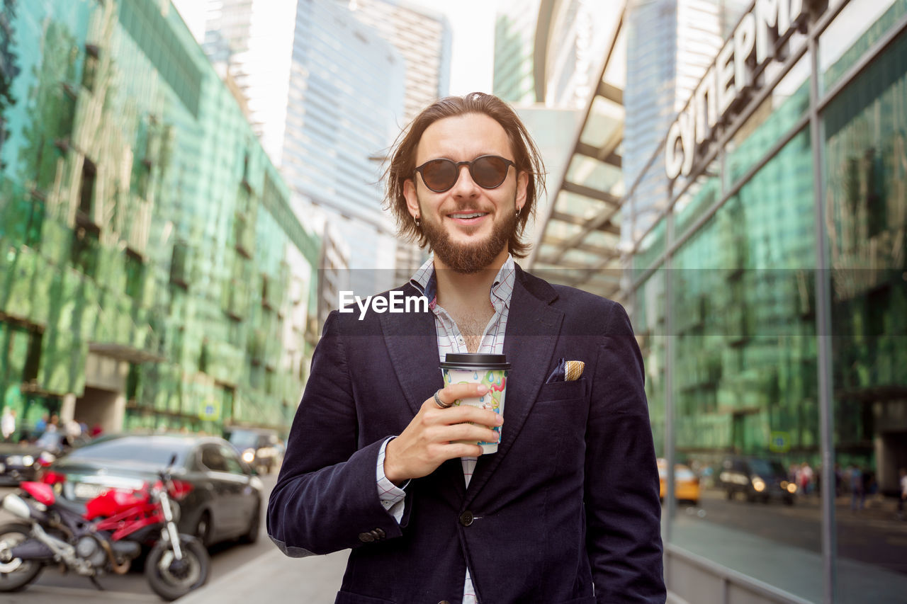 portrait of young man standing against buildings in city